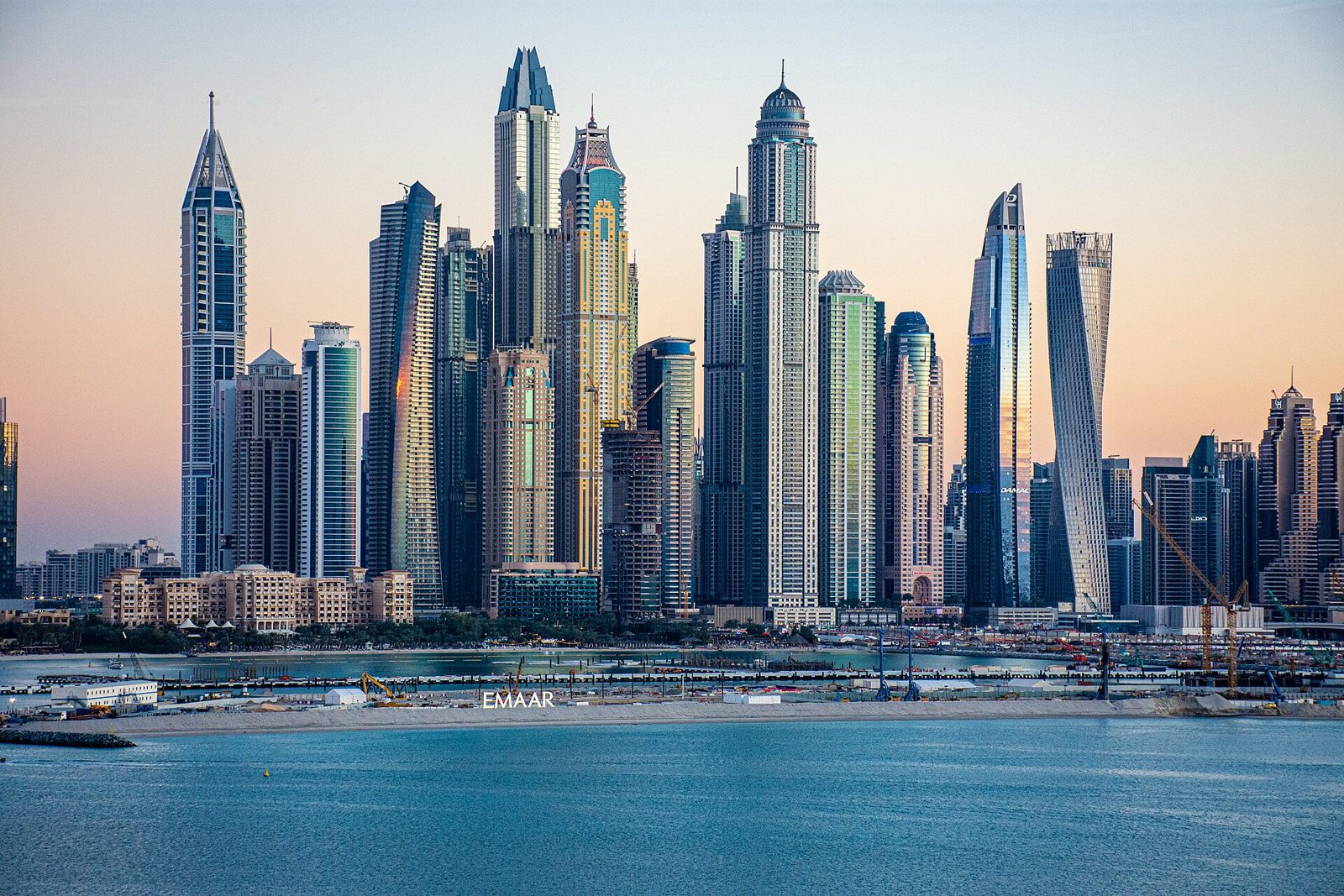 Dubai Marina au coucher du soleil Jet privé Londres Dubaï : les gratte-ciel de Dubai Marina au-dessus de l’eau au coucher du soleil